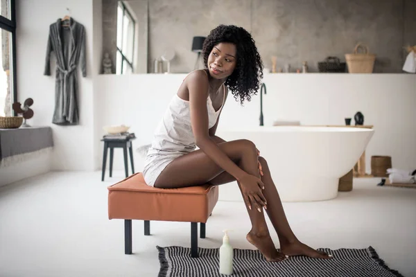 Femme bouclée assise sur une chaise et utilisant de la crème après avoir pris un bain — Photo