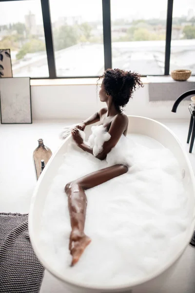 Femme regardant dans la fenêtre tout en étant couché dans le bain avec de la mousse — Photo