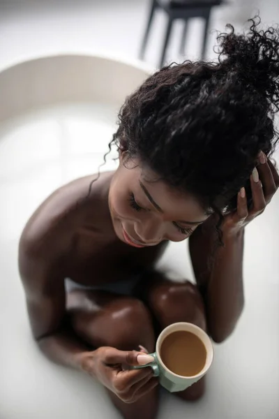 Ansicht von oben lockige sexy Frau sitzt in der Badewanne mit Schaum und genießt Kaffee — Stockfoto