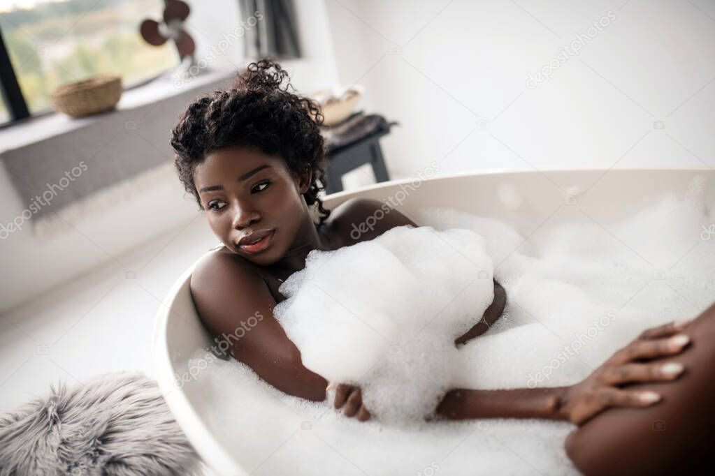 Beautiful African-American woman chilling in bath with foam