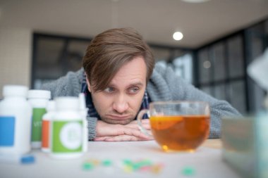 Blue-eyed man feeling sick and tired drinking hot tea clipart