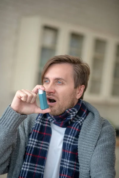 Hombre joven de ojos azules que tiene asma usando inhalador —  Fotos de Stock