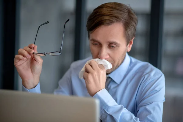 Uomo in camicia blu seduto in ufficio nonostante l'influenza — Foto Stock