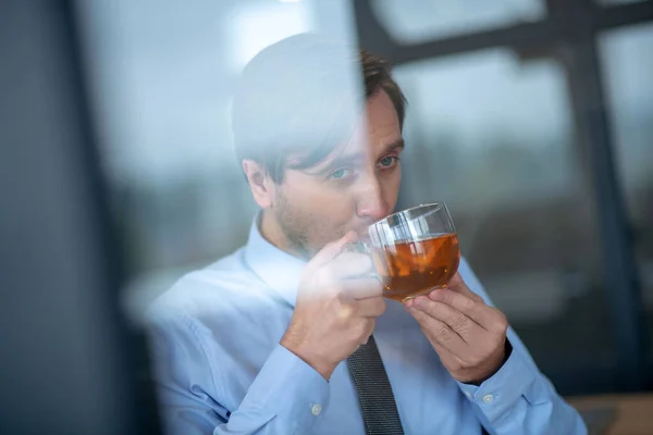 Blauäugiger Geschäftsmann trinkt heißen Tee bei der Arbeit — Stockfoto