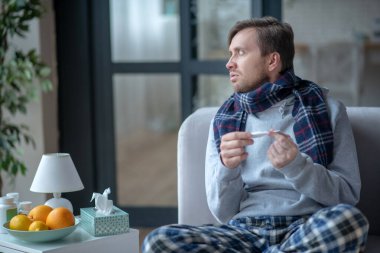 İlaç aldıktan sonra elinde termometre tutan koyu saçlı bir adam.