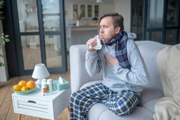 Muž sedí na pohovce a kašle po užití vitamínů — Stock fotografie