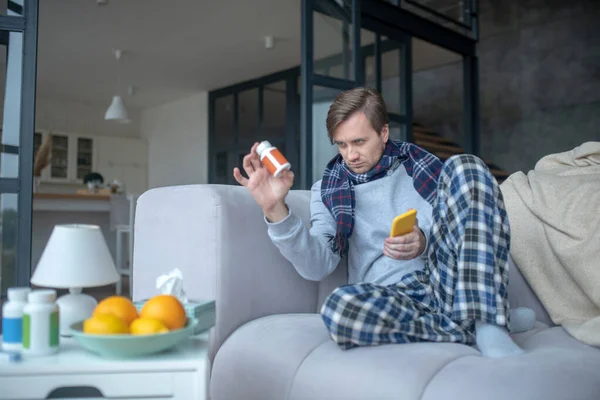 Sick man wearing scarf holding pack of vitamin C