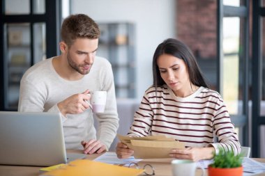 Koca kahve içerken karısı posta kutusunu tutuyor.