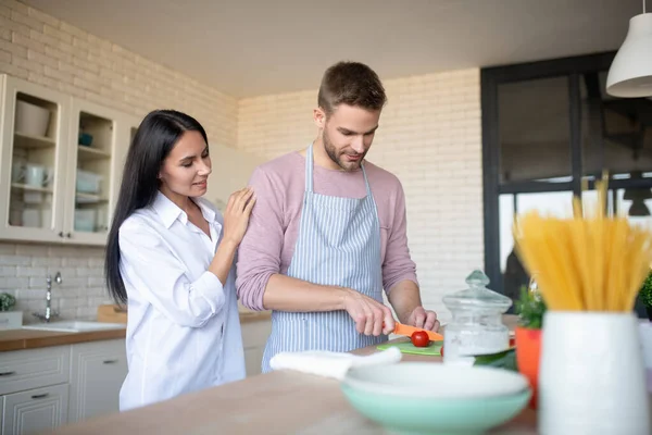 Dunkelhaarige Frau umarmt Ehemann, der Paprika für Salat schneidet — Stockfoto