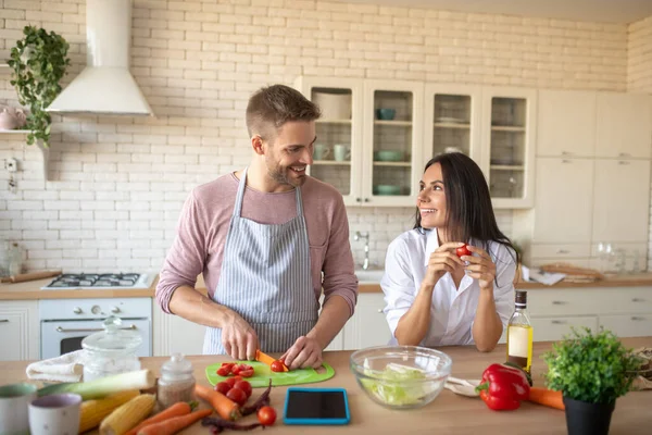 Esposa sonriendo mientras mira a su marido cocinar el desayuno — Foto de Stock