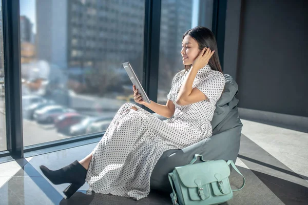 Junge brünette Frau sitzt auf Sackstuhl und liest Zeitung — Stockfoto