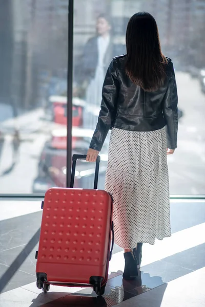 Bruneta žena v kožené bundě chůze s červeným kufříkem — Stock fotografie