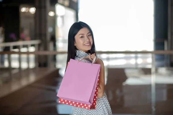 Glad brunett hona bär shoppingväskor på ena axeln, leende — Stockfoto