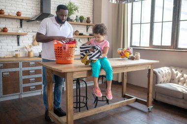 Dark-skinned tall father and his cute daughter speding time at home daling with housework clipart