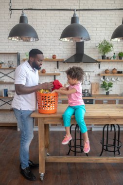Koyu tenli, uzun boylu baba ve tatlı kızı elbiselerini düzenliyor ve meşgul görünüyorlar.