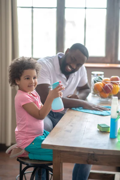 Linda niña con una camiseta rosa sosteniendo un spray, su padre sonriendo —  Fotos de Stock