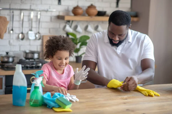 Afroamerikaner mit Bart zieht gelbe Handschuhe an und sitzt neben seiner Tochter — Stockfoto