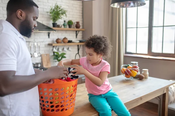 Темношкірий високий батько і його мила дочка сортують одяг для прання — стокове фото