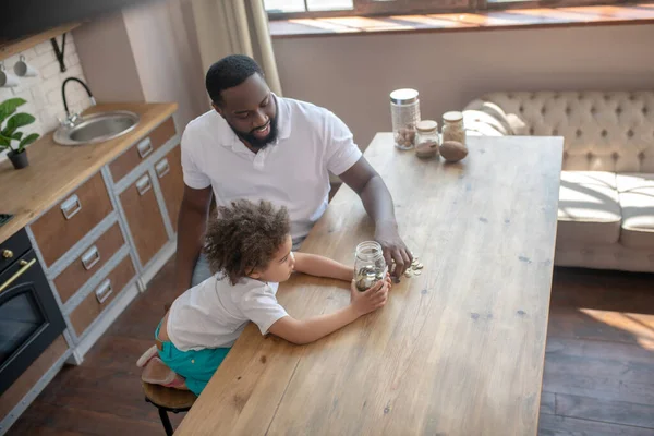 Dunkelhäutiger bärtiger Mann spricht mit seinem Sohn über das Sparen — Stockfoto