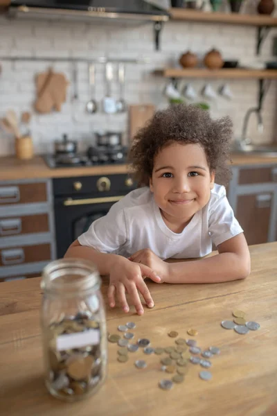 Lindo niño de pelo rizado en una camiseta blanca contando sus ahorros — Foto de Stock