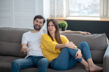 Gülümseyen adam ve hoşnutsuz kız kanepede oturuyor.