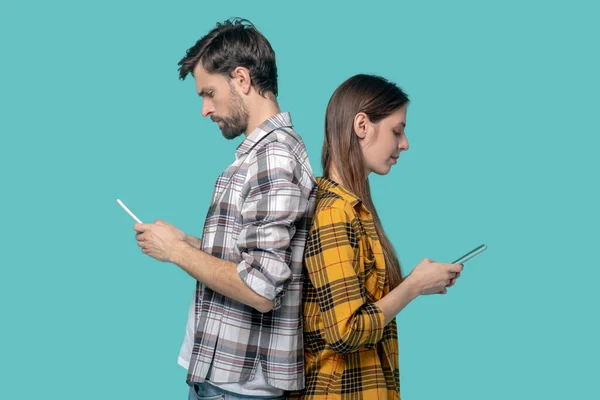 De perfil, una chica y un hombre mirando sus teléfonos inteligentes . — Foto de Stock