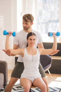 Gülümseyen kadın trisepsi üzerinde çalışıyor ve kocası ona yardım ediyor.