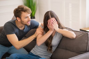 Genç sakallı adam karısına bağırıyor, o da yüzünü kapatıyor ve korkuyor.