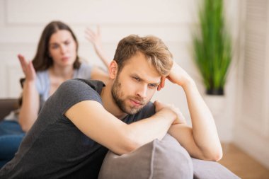 Young bearded man sitting with a depressed look while his wife talking clipart