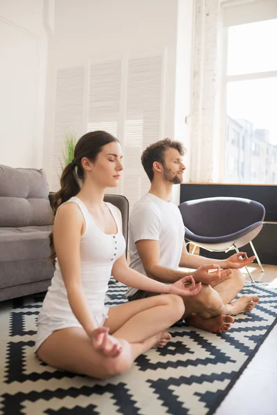 Pareja joven en camisetas blancas sentada en pose de loto y meditando junto con los ojos cerrados — Foto de Stock