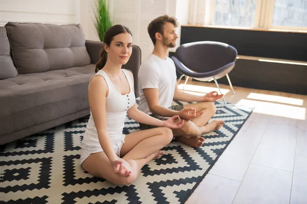 Pareja joven en camisetas blancas sentadas en pose de loto y meditando juntas — Foto de Stock