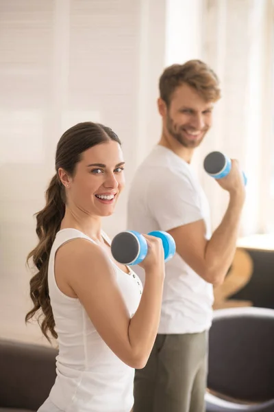 Mujer sonriente haciendo ejercicio con pesas junto con su marido y sintiéndose genial — Foto de Stock