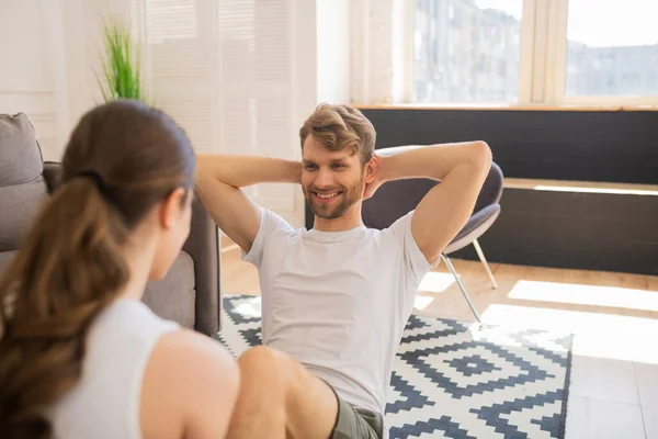 Sonriente hombre barbudo trabajando en sus abdominales y su esposa ayudándole —  Fotos de Stock