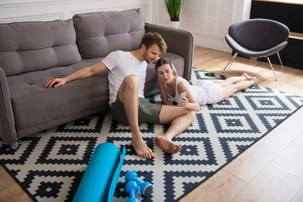 Pareja joven sentada en el suelo después de hacer ejercicio y navegar por Internet —  Fotos de Stock