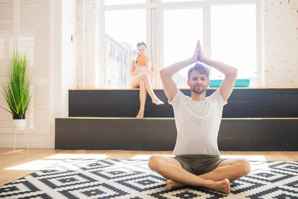 Bearded man in a white tshirt sitting on the floor and meditating with his arms up — Stock Photo, Image