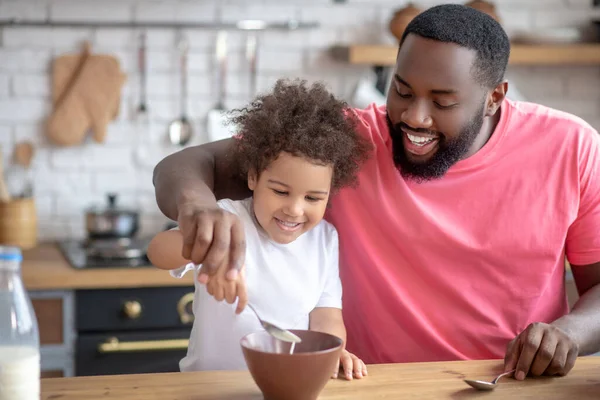 Afroamerikaner mit Bart rührt Milch in Teller seiner Töchter — Stockfoto