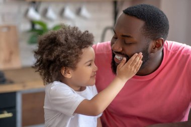 Tatlı küçük kız babasının yüzüne dokunuyor ve mutlu görünüyor.