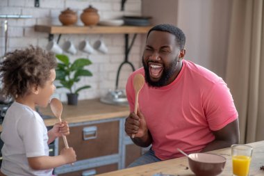 Kıvırcık saçlı tatlı çocuk ve mikrofon olarak kaşık tutan babası harika hissediyor.
