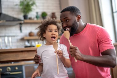 Kıvırcık saçlı şirin bir çocuk ve babasının kaşıklarını tutarak harika bir şarkı söylemesi.