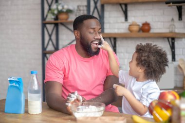 Şirin kıvırcık saçlı çocuk babasının yüzüne un bulaşmış elleriyle dokunuyor ve gülüyor.