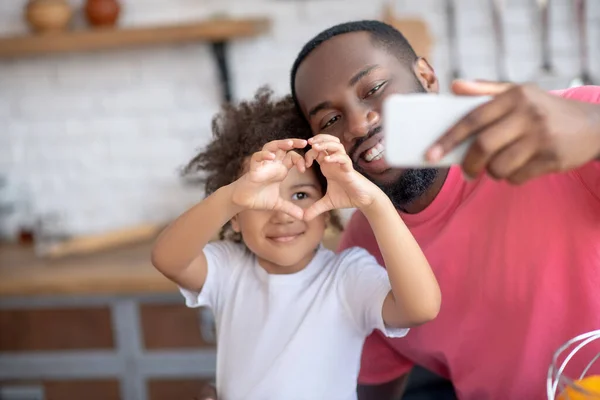 Sladká holčička ukazuje srdeční znamení, zatímco její otec dělá selfie — Stock fotografie