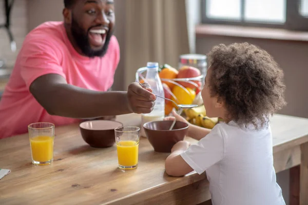 Afroamerikaner im rosa T-Shirt füttert sein Kind — Stockfoto