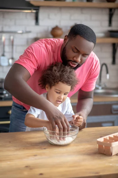 Kıvırcık saçlı şirin çocuk ellerini çiçekle kaseye sokuyor.