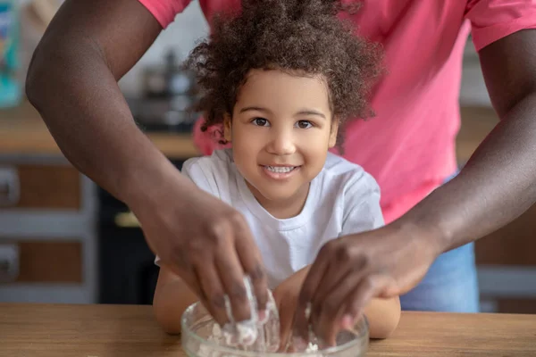 Cute kid with curly hair looking happy putting her hands into the bowl with flower — Stock Photo, Image