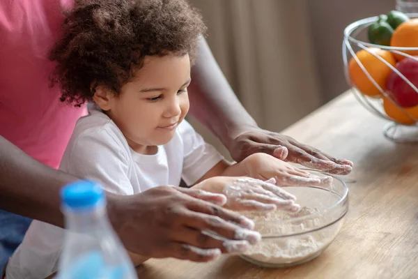 Niedliche kleine Mulatta sitzt am Tisch und bereitet sich darauf vor, mit ihrem Vater zu kochen — Stockfoto