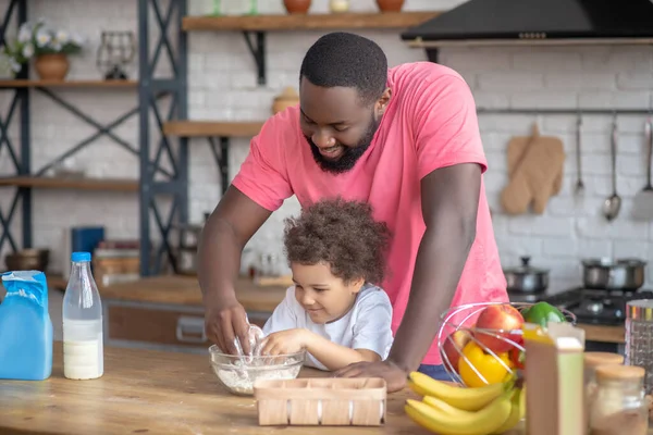 Afroamerikanischer bärtiger Mann spielt mit seiner Tochter, die das Mehl in der Schüssel rührt — Stockfoto