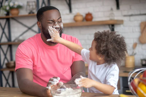 Niedliche lockige Kind berührt ihren Vater Gesicht mit Händen mit Mehl gefärbt — Stockfoto