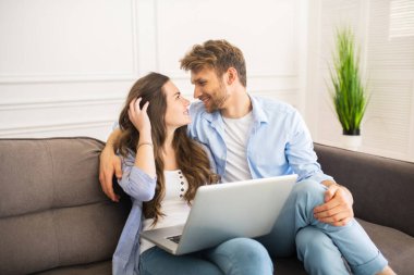 Kot pantolonlu genç bir çift kanepeye oturmuş birbirlerine bakıyor ve mutlu hissediyorlar.