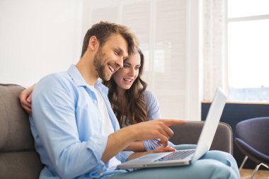 Kot pantolonlu genç bir çift kanepede oturmuş internetten bir şeyler izliyor.