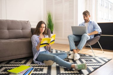 Genç kadın sınava hazırlanıyor, kocası dizüstü bilgisayarla çalışıyor.